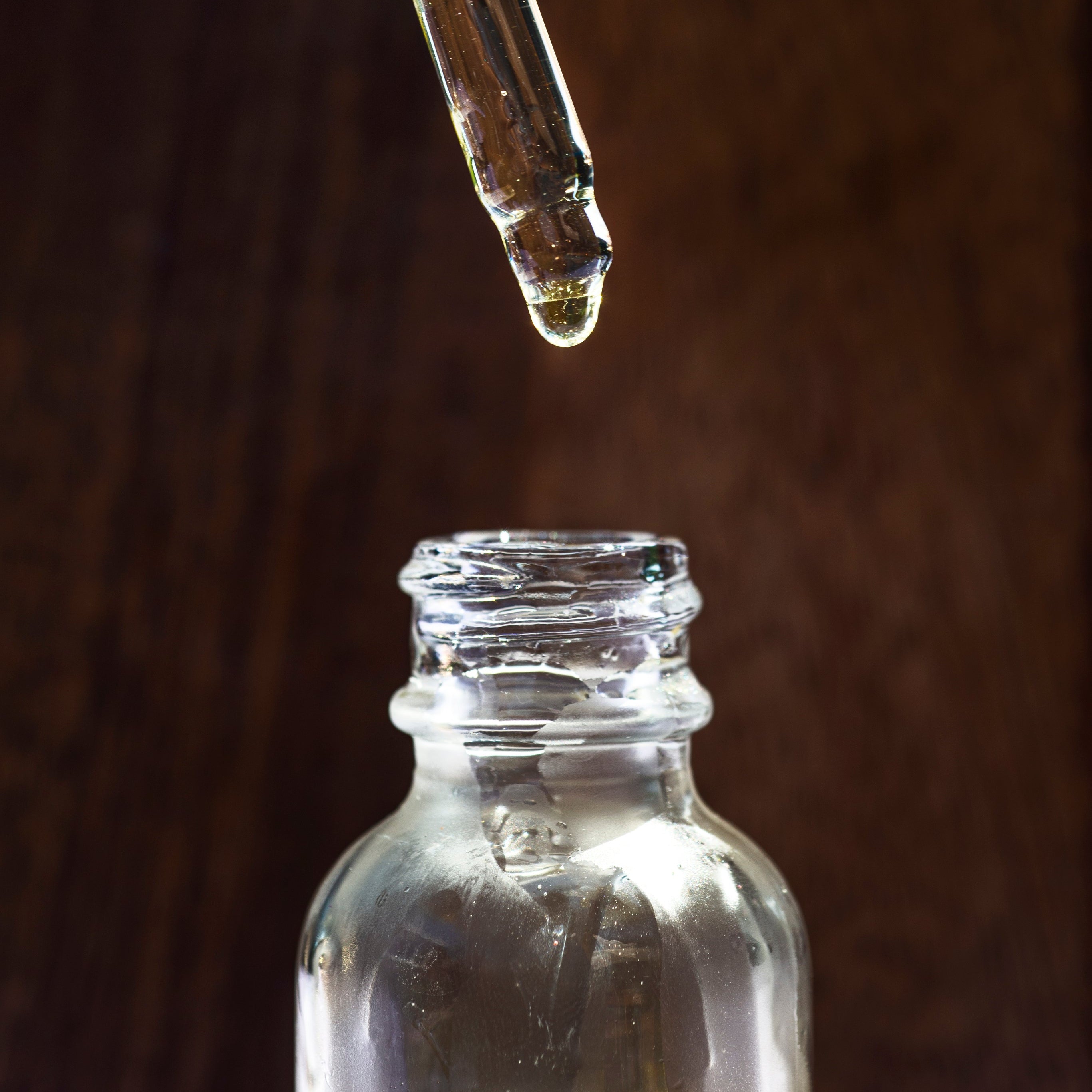 Dropper with liquid being added to a small bottle against a dark background