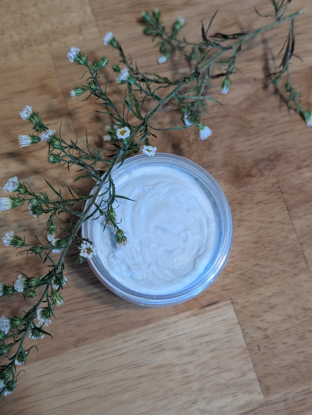 Jar with whipped tallow inside, next to flowers. 