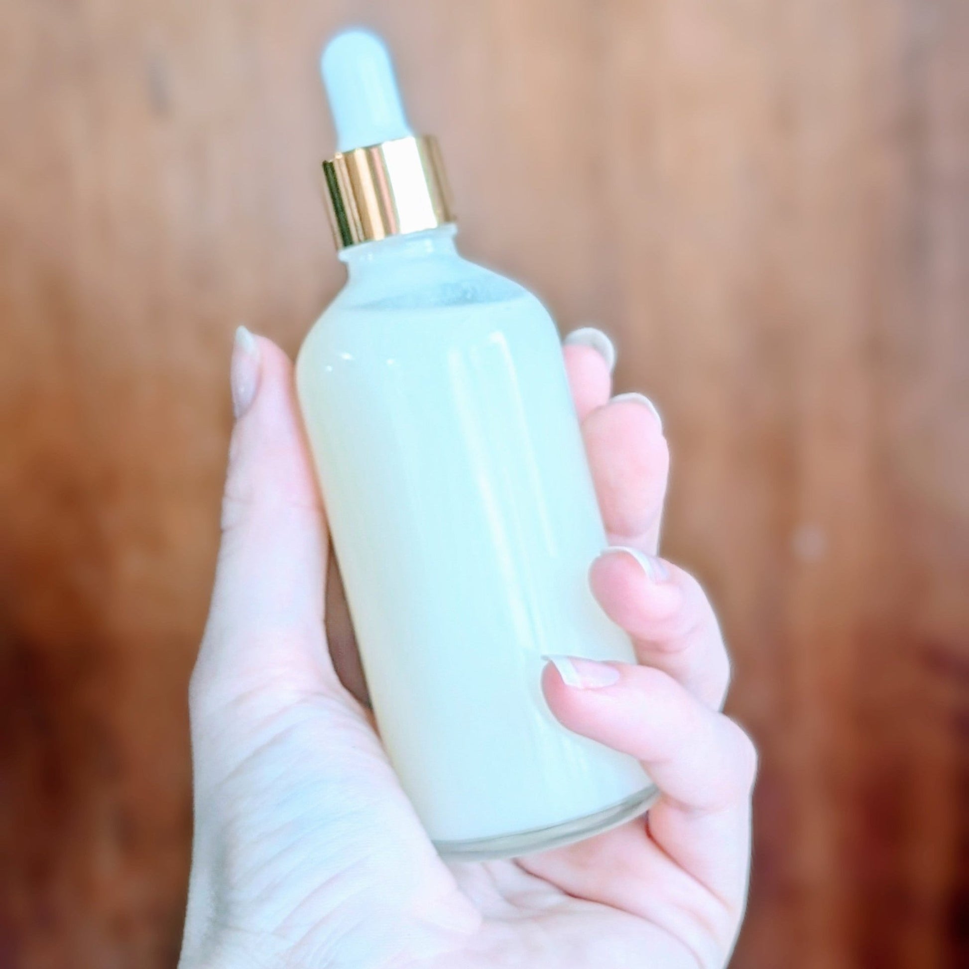 Hand holding a light blue dropper bottle with a gold cap against a wooden background