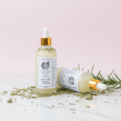 Two bottles of Ceramide Facial Serum with rosemary leaves on a light pink background